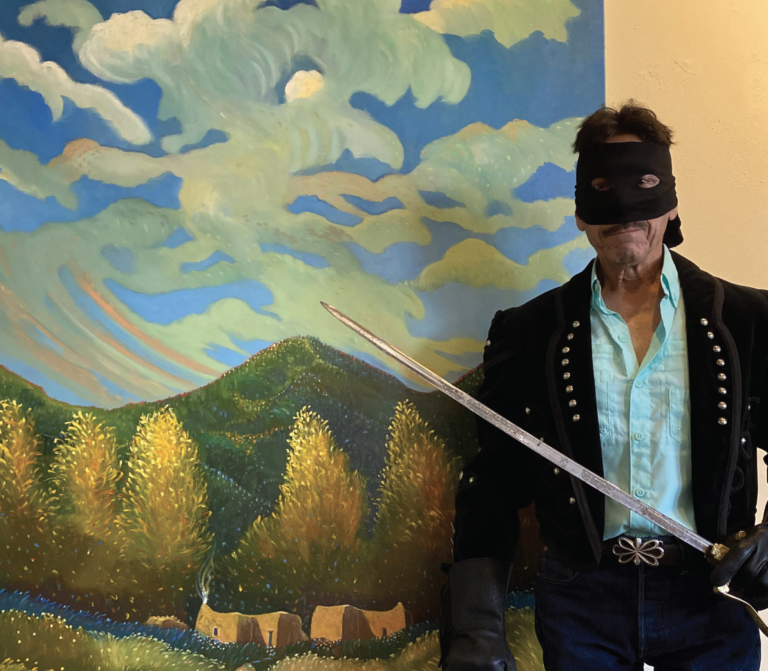 Ed Sandoval, painter and art teacher, stands in front of a painting dressed like Zorro